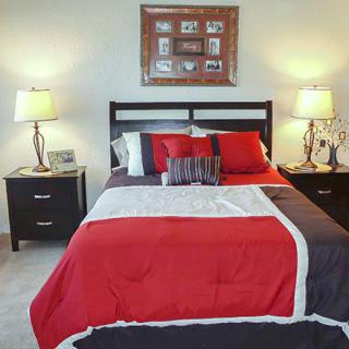 A neatly arranged bedroom with a red, white, and black color scheme, featuring a bed flanked by two lamps on nightstands.