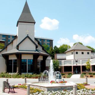 A picturesque building with a tower and a fountain in the foreground, surrounded by a garden and flowers.