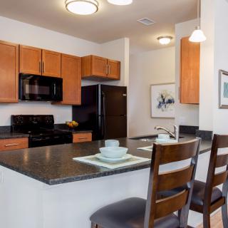 A modern kitchen with wooden cabinets, appliances, and a dining area featuring bar stools at the counter.
