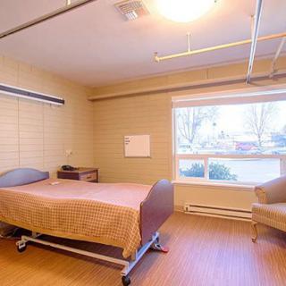 A hospital room with a single bed, large window, and minimal furniture.