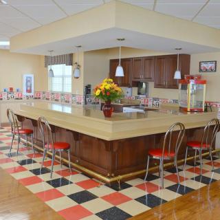 A retro-style kitchen with a central island, red bar stools, and a checkered floor.