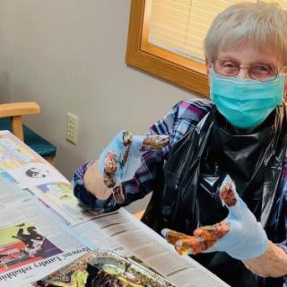 A senior person wearing a mask is engaging in a painting activity indoors.