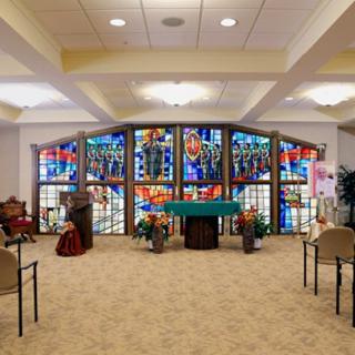 A chapel interior featuring stained glass windows and several rows of seating.