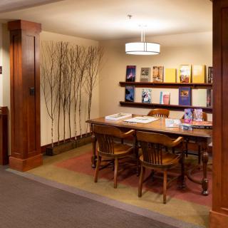 A cozy library reading area with a wooden table, chairs, and a bookshelf filled with books.
