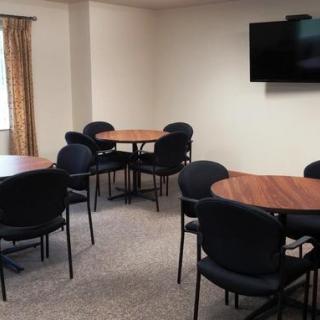 A small meeting room with round tables and chairs, equipped with a wall-mounted television.