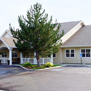A suburban residential building with a tree in front and an adjoining parking lot.