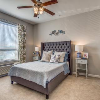 A cozy bedroom with a large window, stylish bed, and matching nightstands under soft lighting.