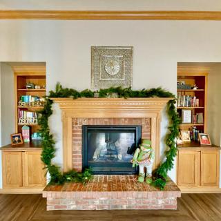 A cozy fireplace adorned with garland and ornaments, flanked by wooden bookshelves filled with books.