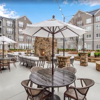 A modern outdoor patio with tables, chairs, and umbrellas in an apartment complex courtyard.