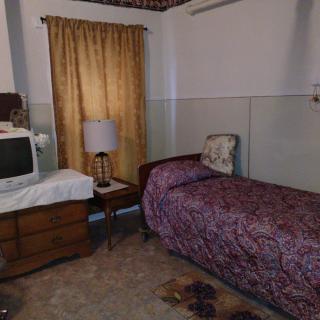 A vintage-styled bedroom featuring a bed, an old television on a dresser, and a lampshade next to gold-colored curtains.