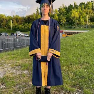 A proud graduate posing in their cap and gown on a sunny day.
