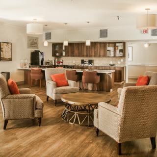 A modern living room with comfortable armchairs, a stylish coffee table, and an open kitchen area featuring wood flooring.