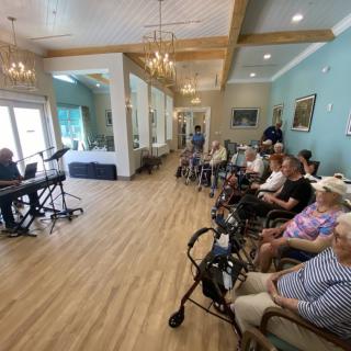 A group of elderly people enjoying a piano performance in a spacious community room.