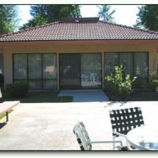 A view of a house with large windows and an outdoor patio area, featuring garden chairs and table.