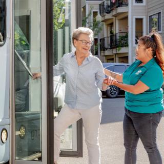 A woman assists an elderly person boarding a bus.