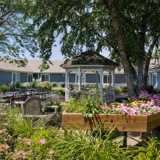 A peaceful garden with a gazebo and vibrant flowers under the shade of trees.