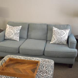A comfortable gray sofa with patterned pillows in a living room setting, accompanied by a wooden tray on an ottoman.