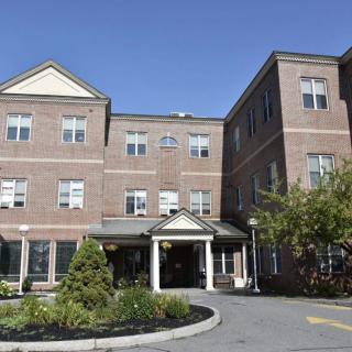 A brick residential building with a landscaped entrance under a clear blue sky.