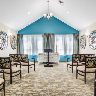 A small chapel interior with arranged chairs, a podium, and decorative windows.