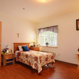 A cozy bedroom with a single bed, decorated with a floral cover and a bedside table with a lamp.