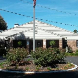 A building with a flagpole in front, surrounded by landscaping and trees under a clear sky.