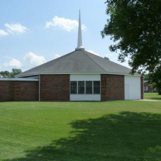 A brick church with a steeple set against a clear blue sky and surrounded by a green lawn.