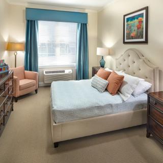 A cozy bedroom with a double bed, upholstered headboard, bedside tables, lamps, and an armchair near the window.