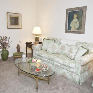 A cozy living room with a floral-patterned sofa, glass coffee table, and elegant artwork on the walls.