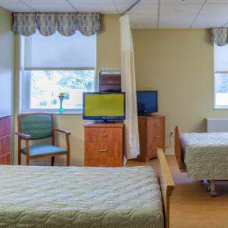 A hospital room with two beds, a television, and a curtain divider.