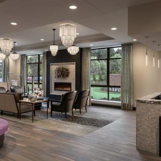 A modern living room with elegant chandeliers, a fireplace, and large windows offering a view of the outdoors.