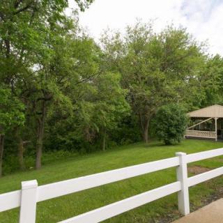 A peaceful outdoor scene with a white fence, lush green trees, and a pavilion.