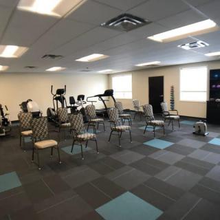 A fitness room with various exercise equipment and chairs arranged in rows.