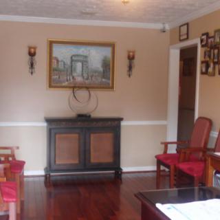 A cozy living room with wooden flooring, featuring a cabinet, red chairs, and a wall painting.