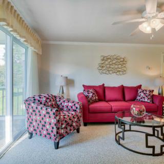 A cozy living room featuring a vibrant red sofa, patterned armchair, and a stylish glass coffee table, illuminated by natural light from large sliding doors.