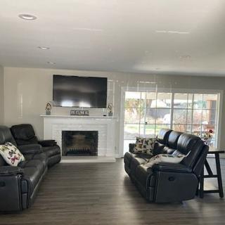 A modern living room with a large television above the fireplace, featuring comfortable sofas and hardwood flooring.