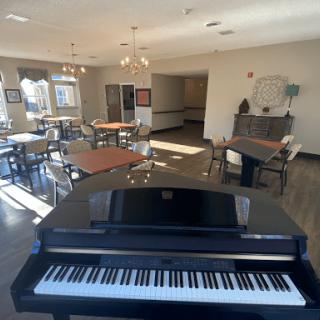A modern lounge with a piano, featuring tables and chairs bathed in sunlight.