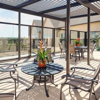 A sunny outdoor patio with tables, chairs, and plants under a pergola.
