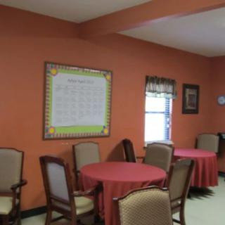 A small dining area with round tables, chairs, and an orange wall displaying a calendar.