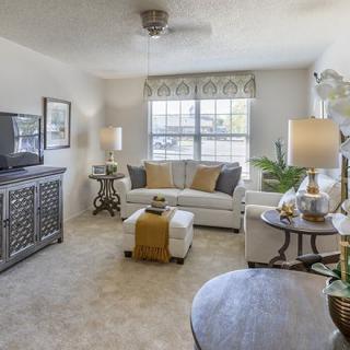 A cozy living room with neutral tones, featuring a sofa, coffee table, TV, and floor lamps.