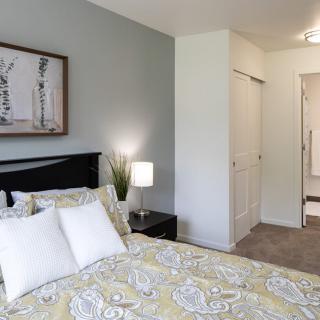 A modern bedroom with a neatly made bed, a nightstand with a lamp, and artwork on the wall.
