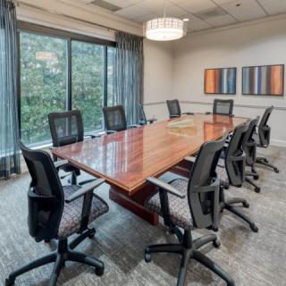 A modern conference room with a large wooden table and ergonomic chairs, featuring large windows and abstract artwork on the walls.