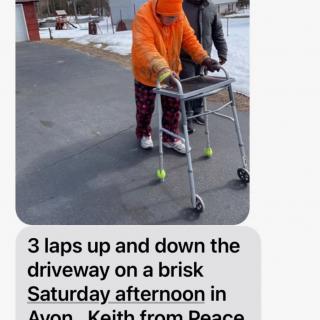 An elderly person walking with a walker on a driveway during a brisk Saturday afternoon.