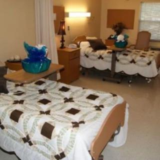 A hospital room with two beds, each covered with quilted bedspreads, designed for accessibility.