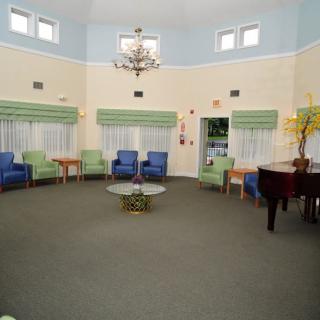 A spacious room with arranged seating, a piano, and a chandelier.