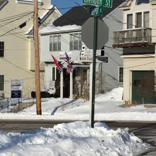 A snowy urban scene featuring street signs and flags displayed in front of residential buildings.