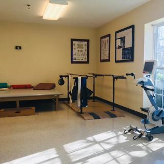 A rehabilitation room equipped with a therapy bed, parallel bars, and exercise equipment.