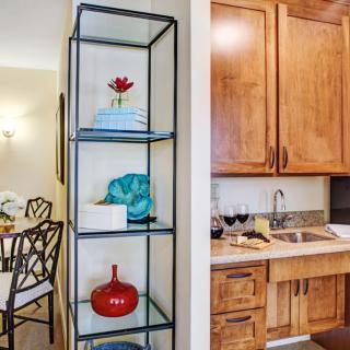 A cozy kitchen corner with wooden cabinets, decorative shelves, and a view of the dining area.