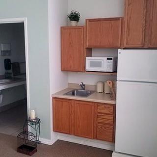 A small apartment kitchen with wooden cabinets, a refrigerator, microwave, and a sink.