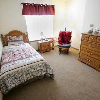 A cozy bedroom with a single bed, wooden furniture, and red curtains.