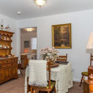 A cozy dining room with vintage wooden furniture, featuring a table set with a lace tablecloth and a hutch displaying decorative items.